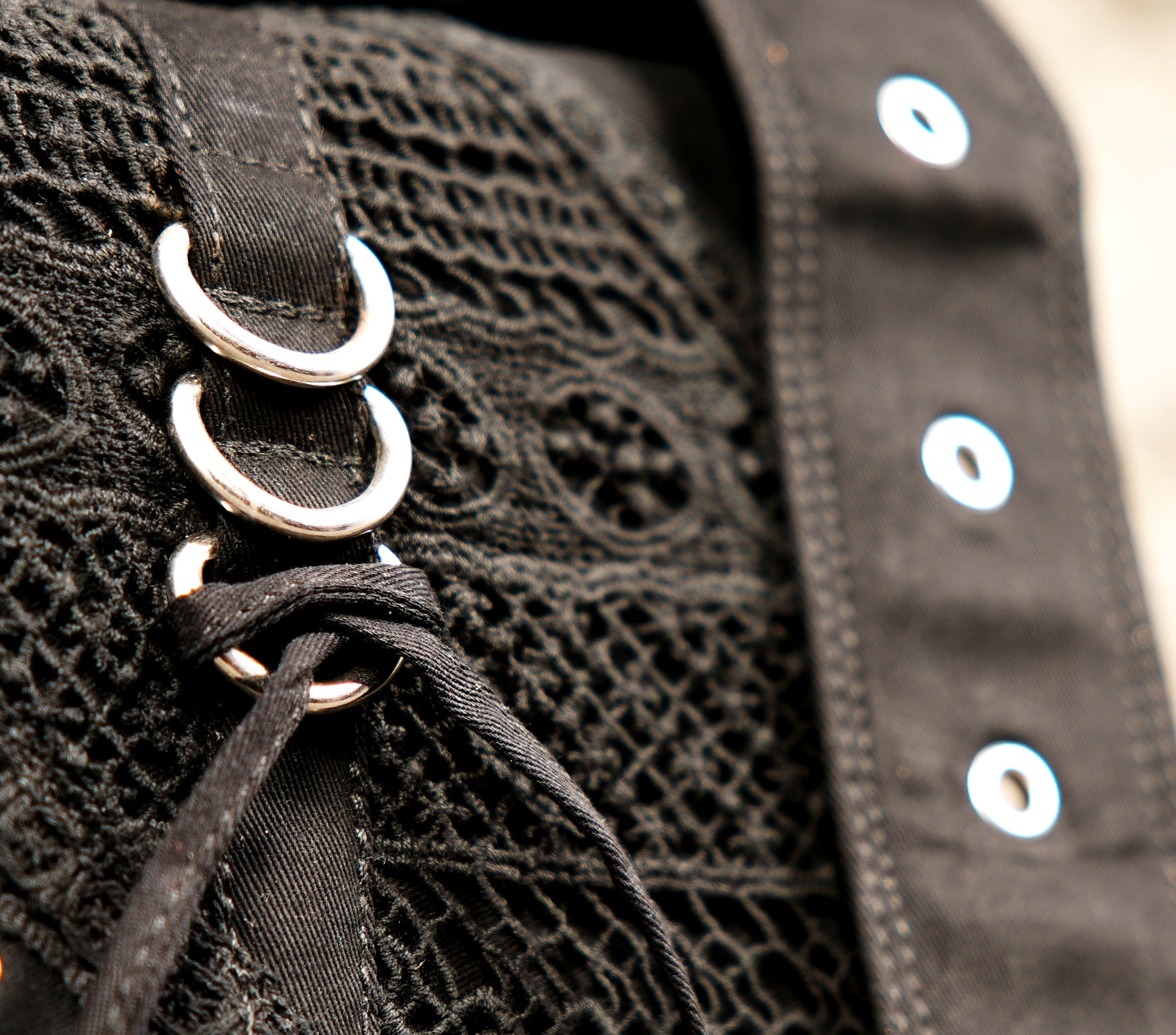 Gothic-inspired black utility fanny pack with a distinct lace-up mesh central pocket and metal accents.