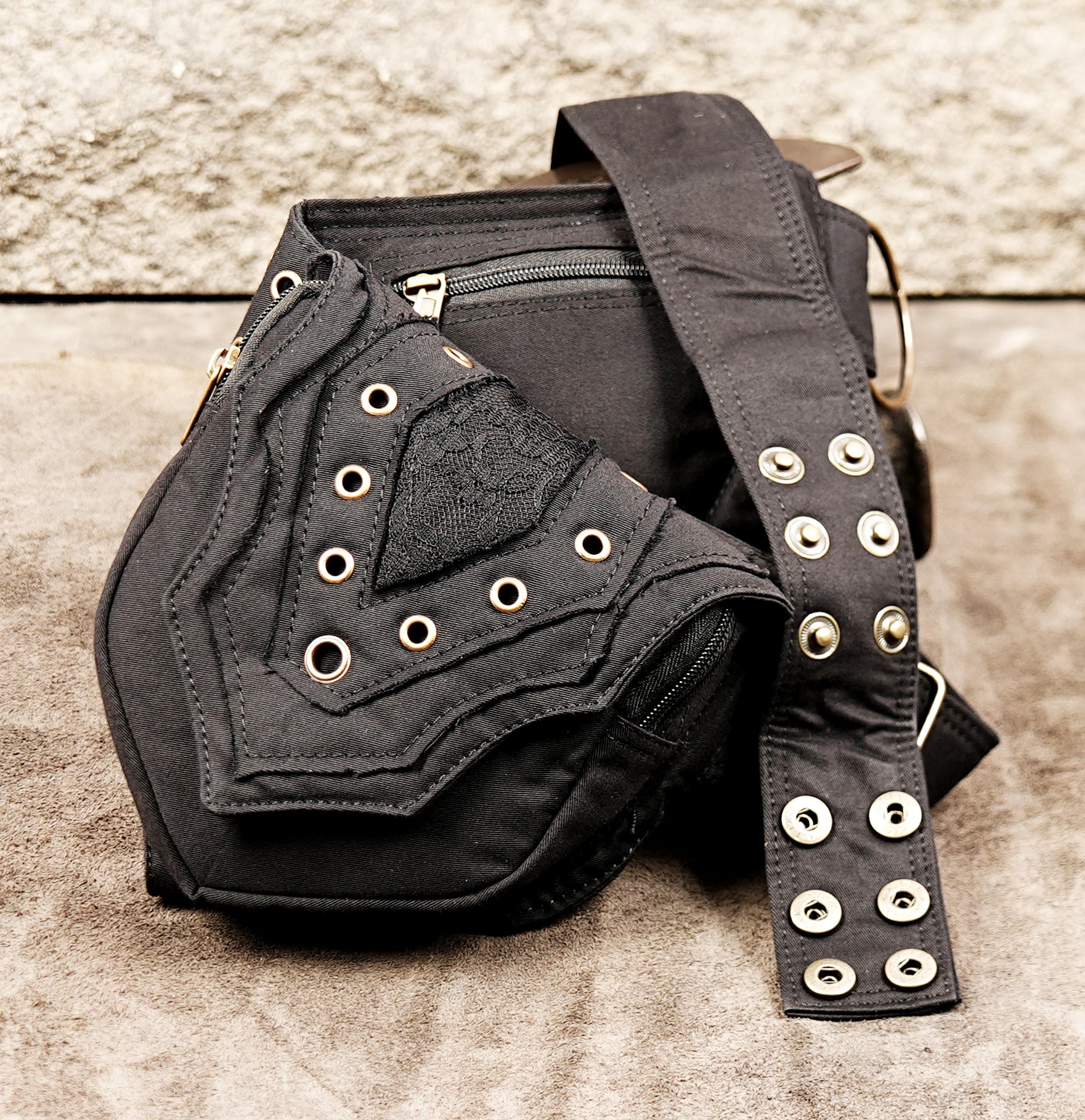 Studded black fanny pack with pointed pocket flaps and brass details