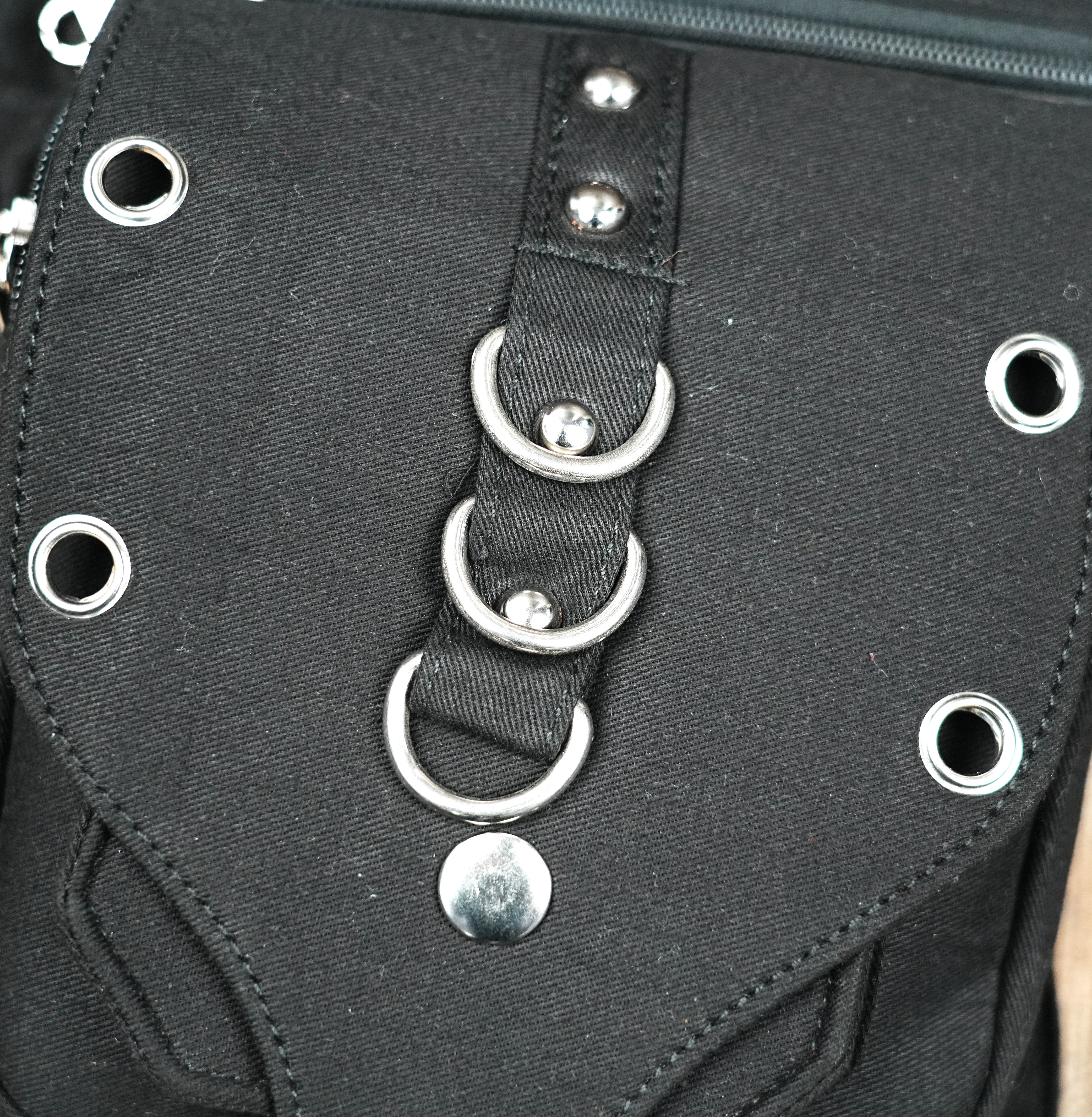 "Heavy-duty black canvas hip bag featuring a distinctive studded front panel with three large silver rings and industrial grommets." (USA/Australia)