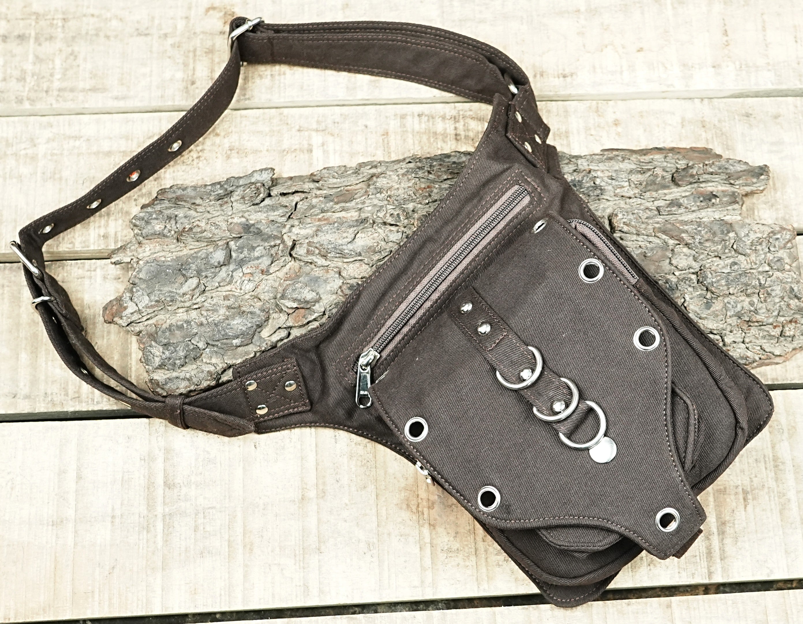 "Alternative black canvas festival belt bag with a distinctive gothic style, including a front flap adorned with metal rings and eyelets." (Europe)