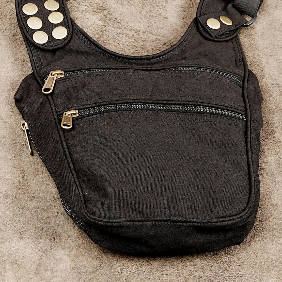 A black canvas shoulder bag with gold-tone hardware, featuring multiple zippered pockets and a padded shoulder strap