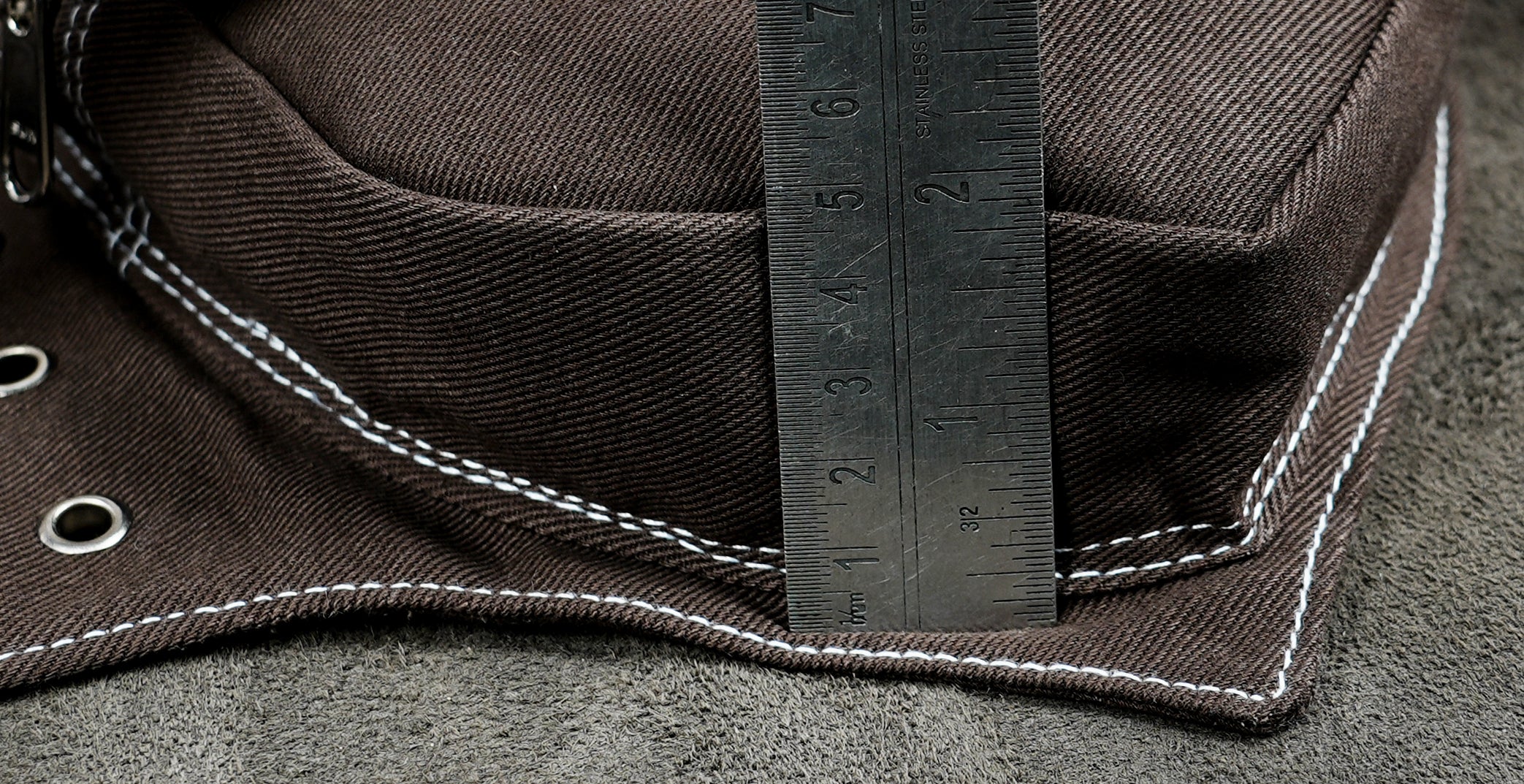 Close-up of a dark brown canvas hat with white contrast stitching and metal grommets