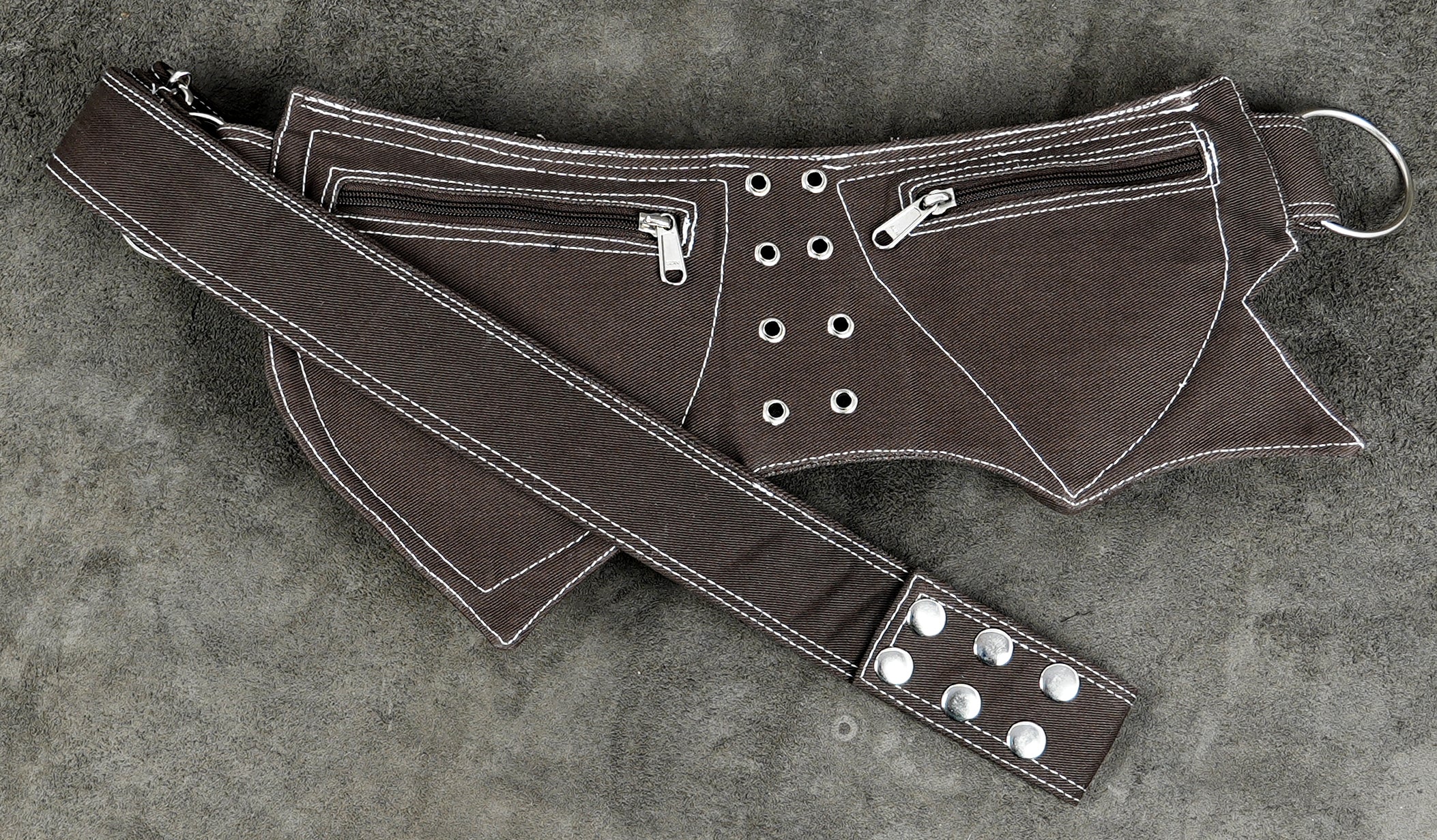 A dark brown belt with white contrast stitching, silver metal grommets, and a matching adjustable cotton strap