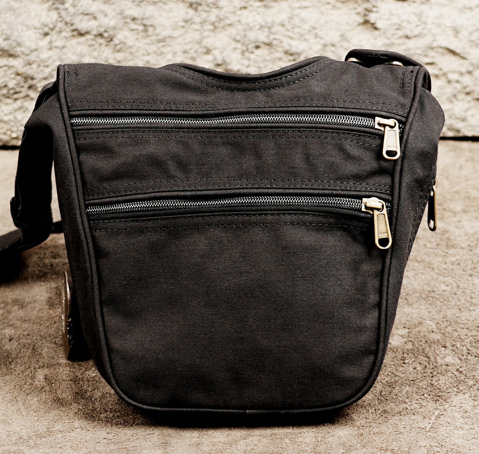 A black canvas crossbody bag with multiple zippered pockets and gold-tone hardware