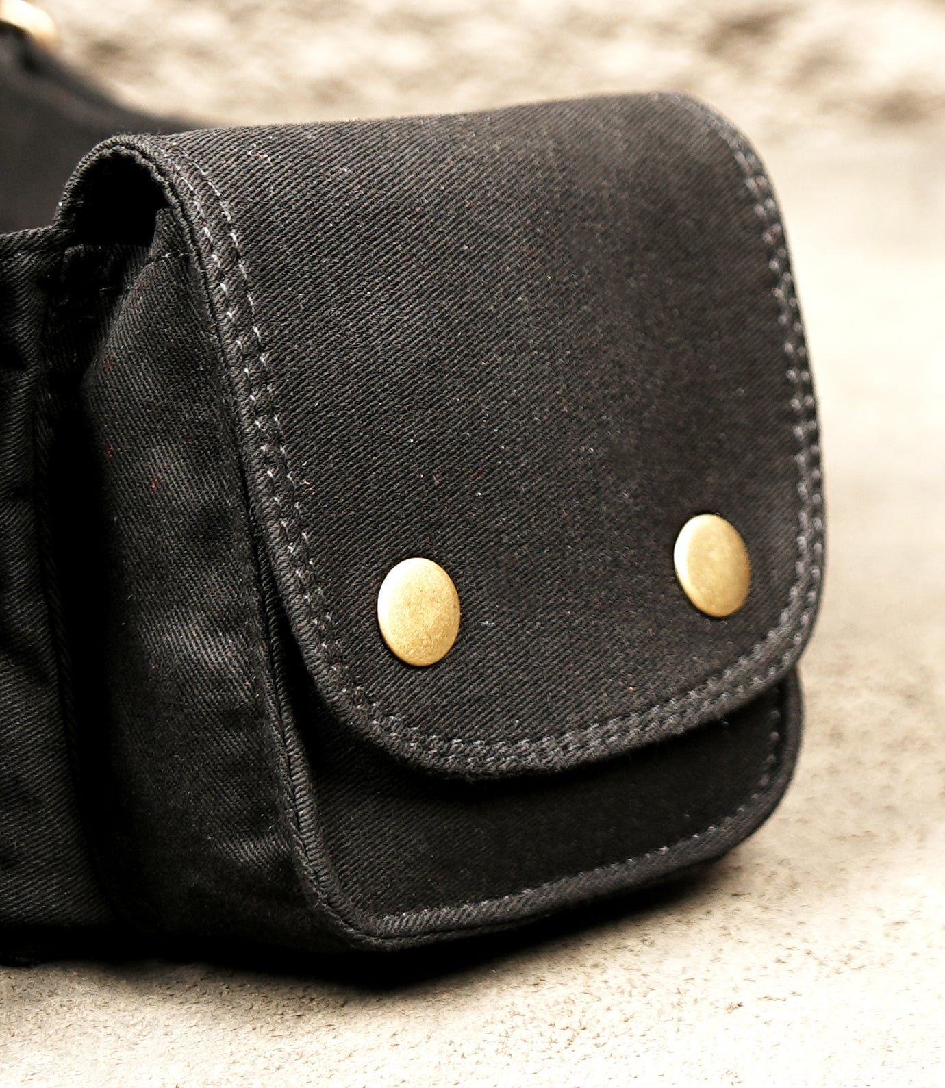 Multi-pocket black cotton fanny pack belt laid flat on concrete