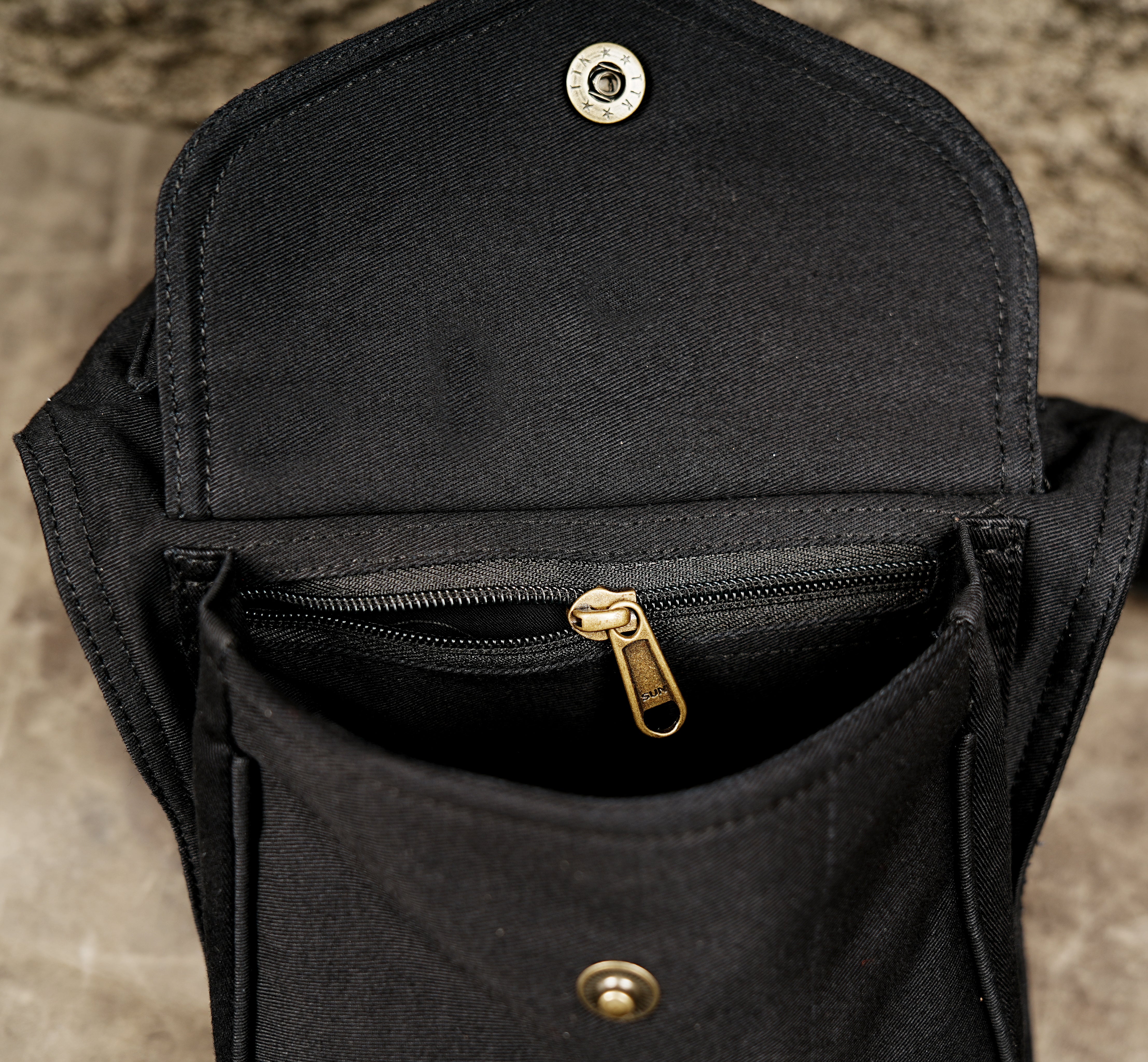Black festival hip bag with flap pocket and brass button detail.